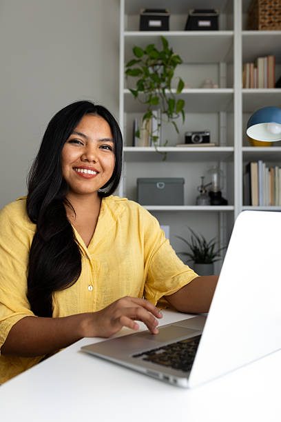 Portrait of a smiling young latin business woman working at home office using laptop