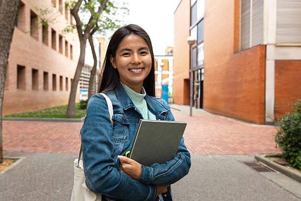 istock Young female student smiling at university campus holding book and bag 2230761983