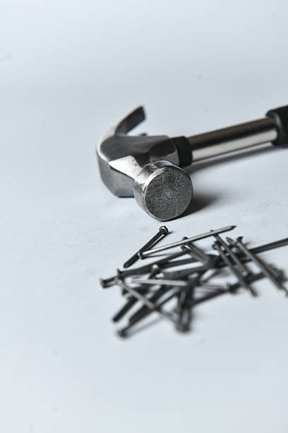 Hammer Placed Beside Straight Metal Nails On White Background