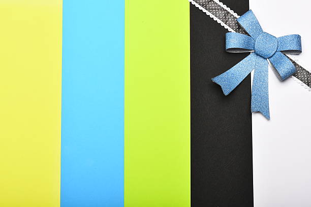 Present wrap with bow in corner. Blue bow on dotted dark ribbon. Gift and celebration concept. Handmade decoration on colourful striped background.