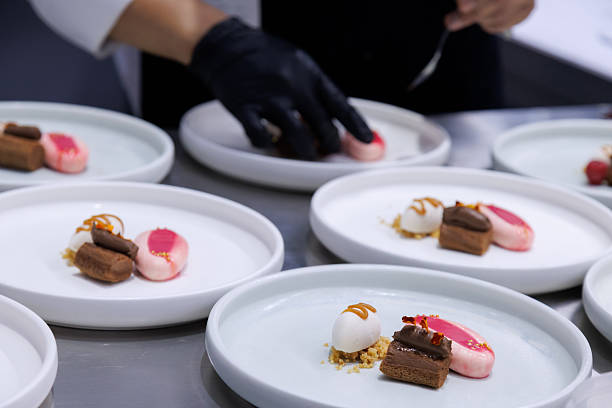 istock plated desserts in professional restaurant kitchen. chef arranges chocolate cake, mousse, and artistic garnishes on plates. fine dining presentation, culinary art and gourmet food preparation. 2230777567