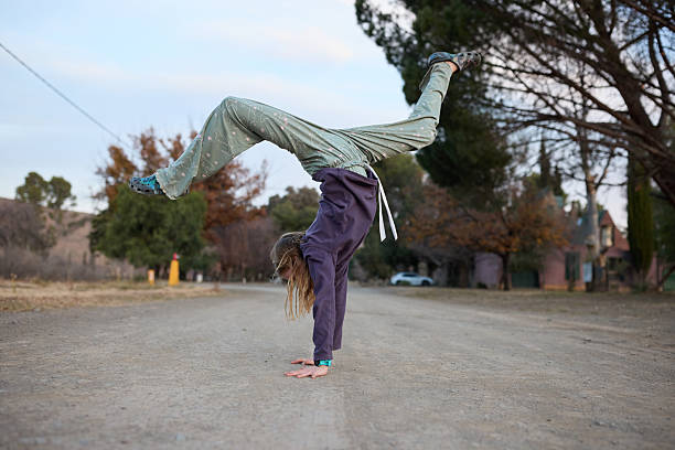 A young girl performs a hand stand on a piece of gravel. She is agile and athletic.