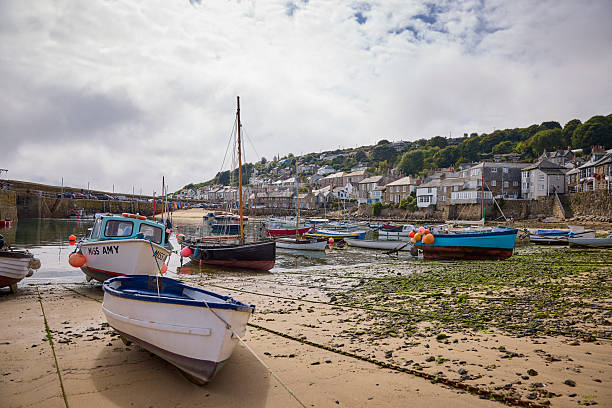 Mousehole harbour and village, with boats moored at low tide, Cornwall, England