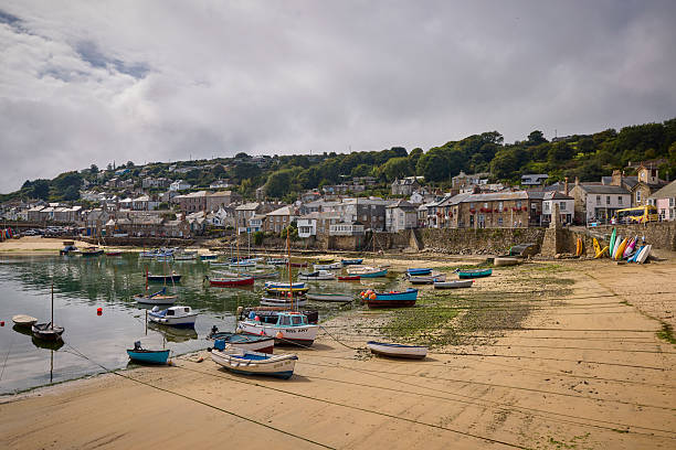 Mousehole harbour and village, with boats moored at low tide, Cornwall, England