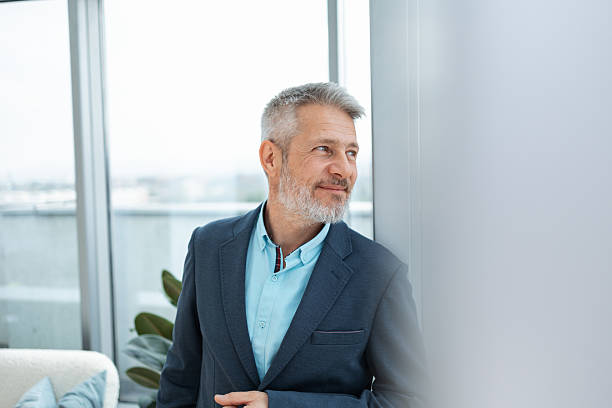 istock Confident middle-aged man in formal attire looking thoughtfully out a window 2230780845