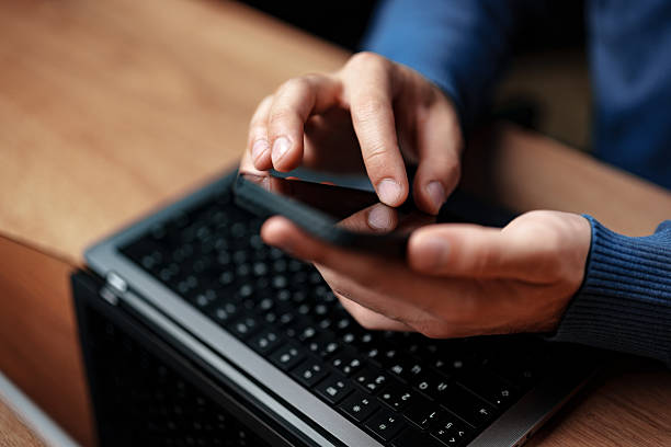 istock Man using smartphone while working on laptop at a wooden desk in a cozy indoor setting during daytime 2230781655