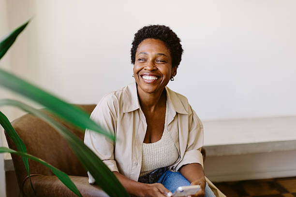 istock Black Brazilian woman smiling and using smartphone on sofa 2230782598