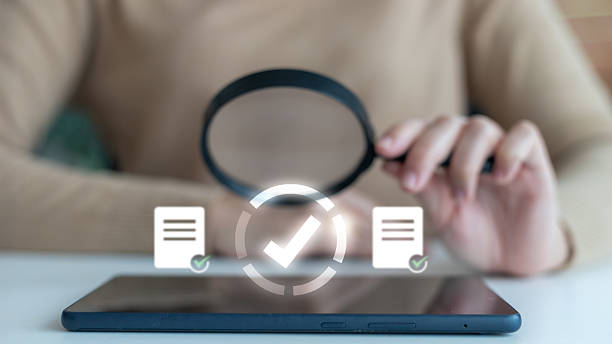 istock Close-up of a person using a magnifying glass over a tablet with floating document and checkmark icons. Concept of digital document verification, data validation, 2230787084