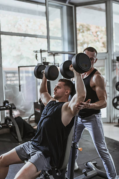 istock Male Fitness Instructor Assisting Client During Dumbbell Shoulder Press Exercise At Gym 2230791959