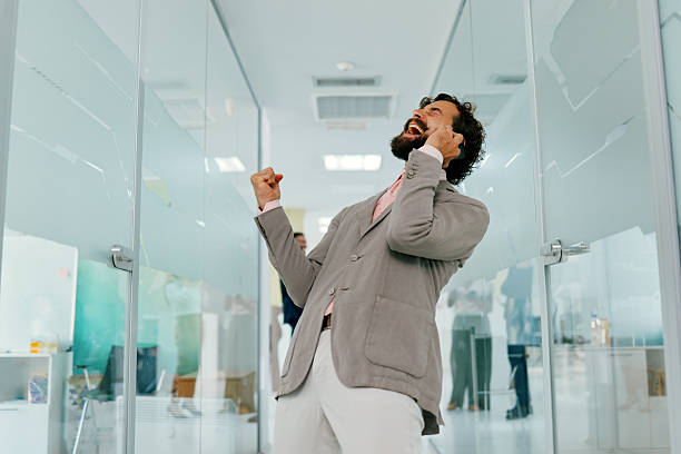 istock Businessman expressing joy while talking on smartphone, celebrating achievement in office 2230793506
