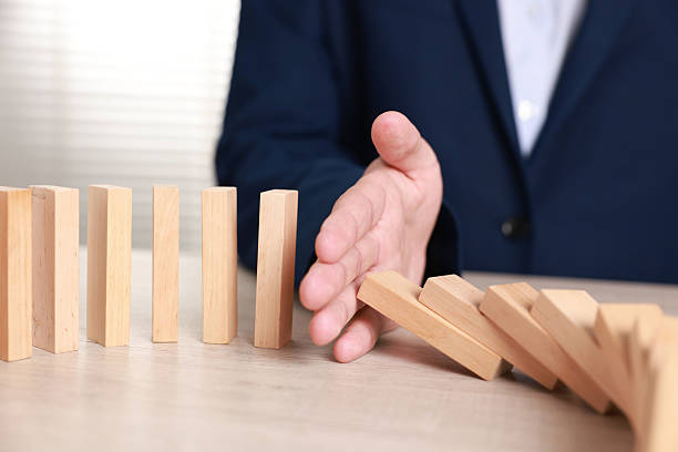 istock Man stopping wooden blocks from falling at table, closeup. Domino effect 2230798480