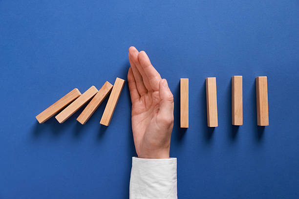istock Man stopping wooden blocks from falling on blue background, top view. Domino effect 2230798687