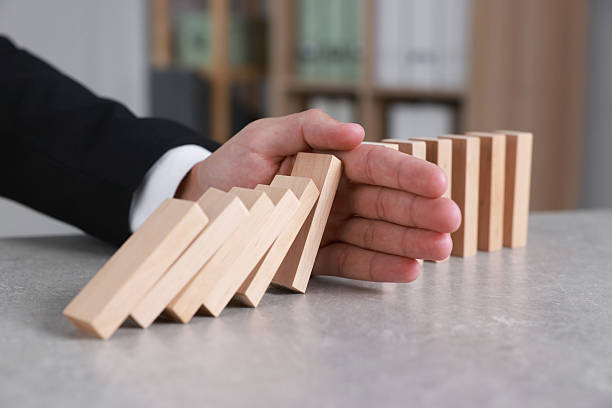 istock Man stopping wooden blocks from falling at table, closeup. Domino effect 2230798715