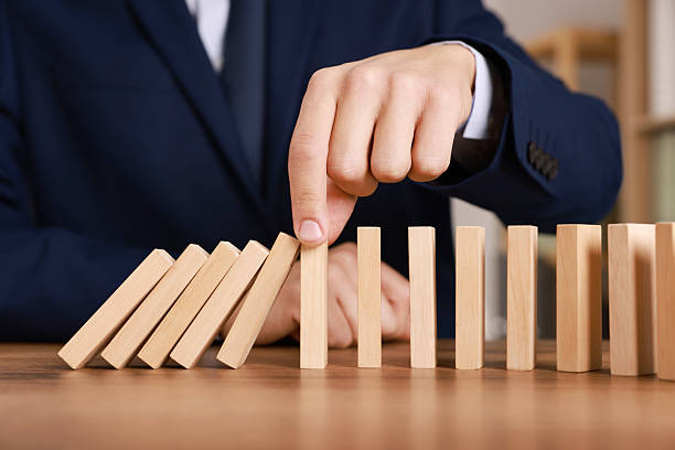 istock Man stopping wooden blocks from falling at table, closeup. Domino effect 2230798736