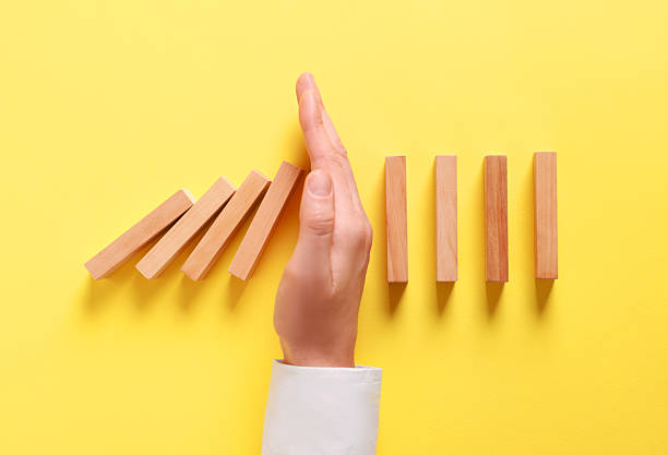 istock Man stopping wooden blocks from falling on yellow background, top view. Domino effect 2230798792