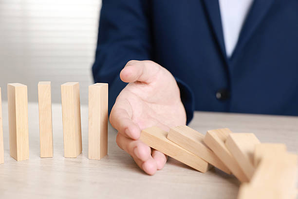 istock Man stopping wooden blocks from falling at table, closeup. Domino effect 2230798844