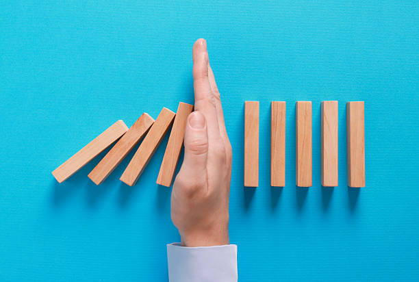 istock Man stopping wooden blocks from falling on light blue background, top view. Domino effect 2230798896
