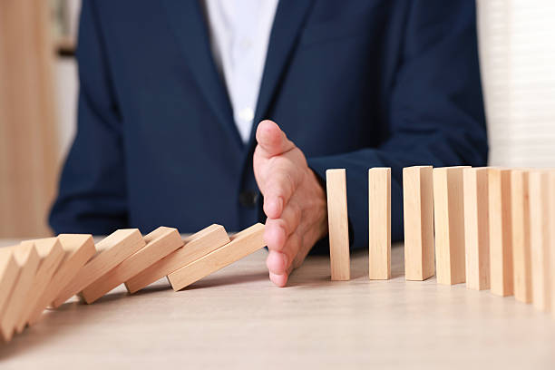 istock Man stopping wooden blocks from falling at table, closeup. Domino effect 2230798934