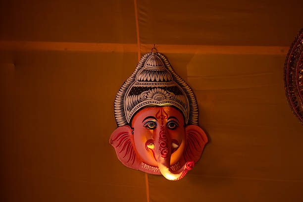 Handmade colorful face mask of god ganesh souvenir hanging on plain black background. Selective focus on object.