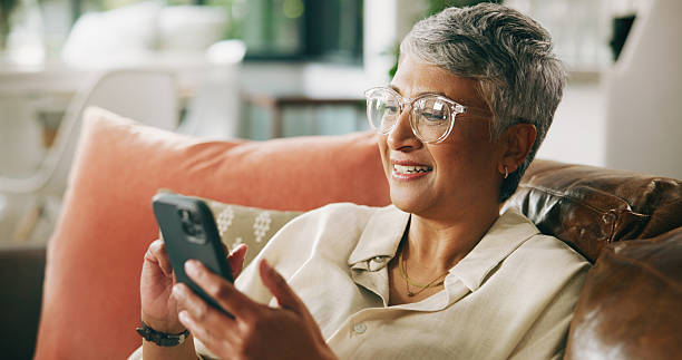 istock Mature woman, phone and happy on sofa with post, texting and check notification on web in home. Person, smartphone and smile with mobile app, click and relax with social media on couch at apartment 2230802058