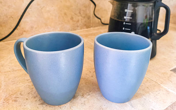 Two 2 blue coffee cups and black coffee maker from Mexico on cream background in clean kitchen.