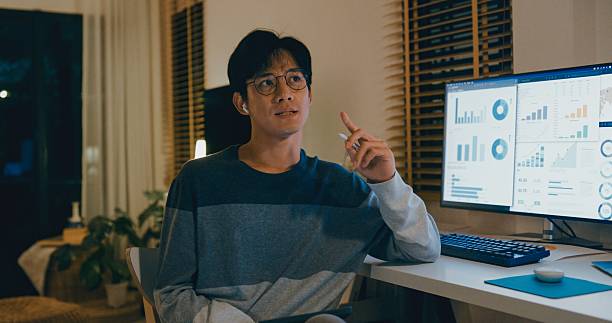 istock Young Asian man financial advisor working late at home, using tablet and laptop, discussing strategy with clients via video call, showcasing remote work efficiency. Remotely and finance. 2230806050
