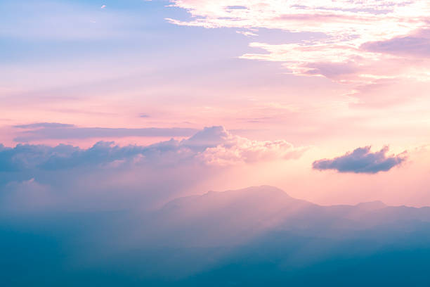 Beautiful pastel-colored sunset illuminating majestic mountain peaks through a layer of clouds, creating a breathtaking and serene natural landscape