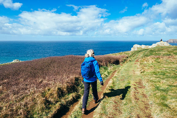 Senior woman walking the coastal path from Lizard Point to Kynance Cove, Cornwall, England.