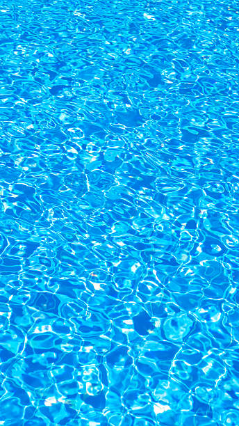 Sunlight reflecting on gently rippling water surface of a swimming pool creates a mesmerizing display of light and shadow, ideal for summer and travel themes