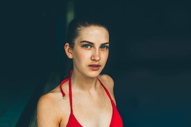 A woman stands elegantly in a flowing red dress, striking a pose in front of a window
