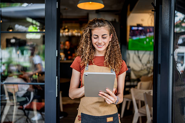 istock Smiling waitress using digital tablet at cafe doorway 2230817608