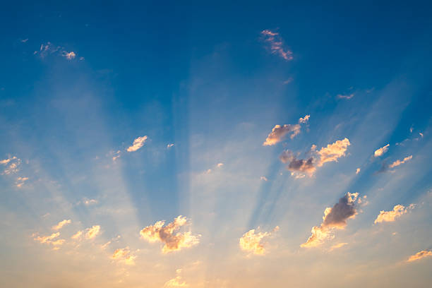 Golden sunbeams are radiating through scattered clouds, creating a mesmerizing spectacle in the vast expanse of the twilight sky during a breathtaking sunset