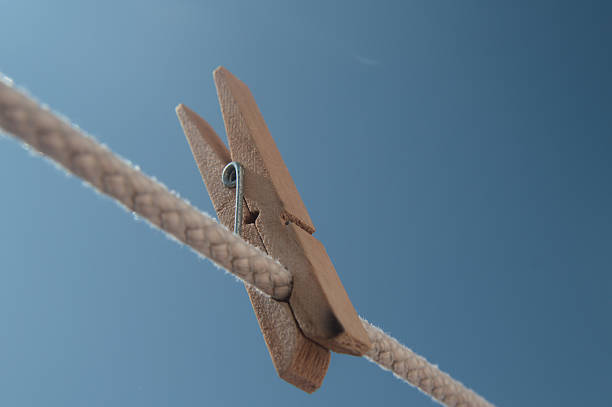 Minimalist photograph of a wooden clothespin on a clothesline with a clear blue sky background. Perfect for concepts of simplicity, domestic life, summer, air drying, freshness.