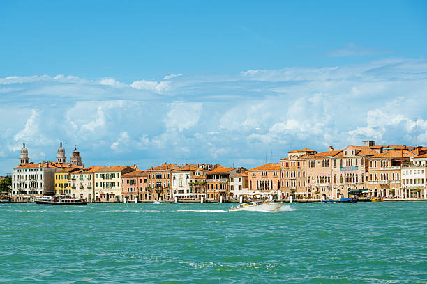 A scenic view of Venice, Italy, showcasing colorful historic waterfront buildings beneath a rich blue sky and fluffy clouds.