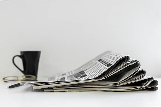 Cup of coffee eyeglasses and pile of newspapers on table