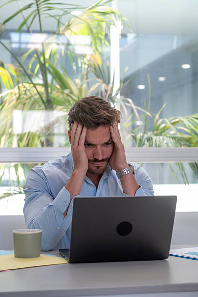 istock Stressed businessman holding head in hands at office desk 2230830110
