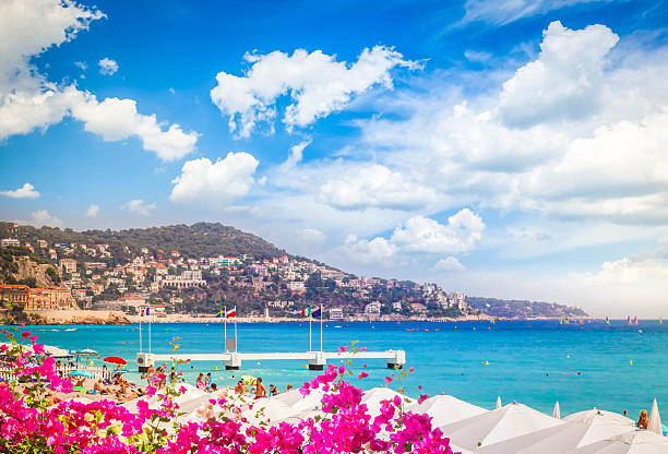 Nice, France - April 28, 2023: A beach along the Mediterranean coast and the buildings of the city seen from behind palm trees.