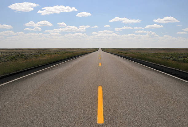 istock Empty rural two-lane highway receding into a horizon with a blue sky with small white clouds. 2230834666