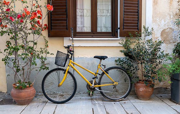 istock Yellow bicycle with a front basket parked infront of a rustic wall with open wooden shutters, potted plants and flowers, Nafplio city street scene 2230841205