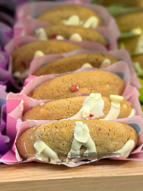Full frame image of row of freshly baked raspberry cheesecake cookies wrapped in a paper bag on wooden parchment paper lined bakery shelf, elevated view, focus on foreground