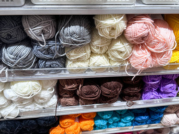 Full frame image of retail shelving wall unit containing multicoloured yarn, shelves full of grey, cream, pink, yellow, white, brown, purple, orange and blue balls of wool for sale, focus on foreground