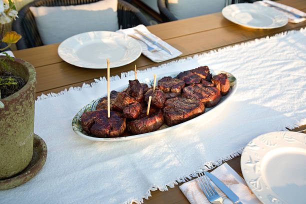 Stock photo showing close-up, elevated view of browned, stuffing meatballs and sausages wrapped in bacon cooked on an oven tray lined with greaseproof parchment paper.