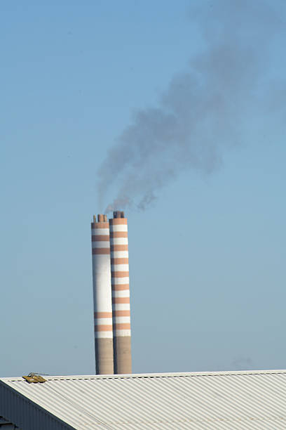 A powerful image of industrial chimneys emitting thick black smoke into the sky, highlighting the environmental impact of emissions. The dark smoke contrasts with the sky, creating a striking and impactful visual of pollution.