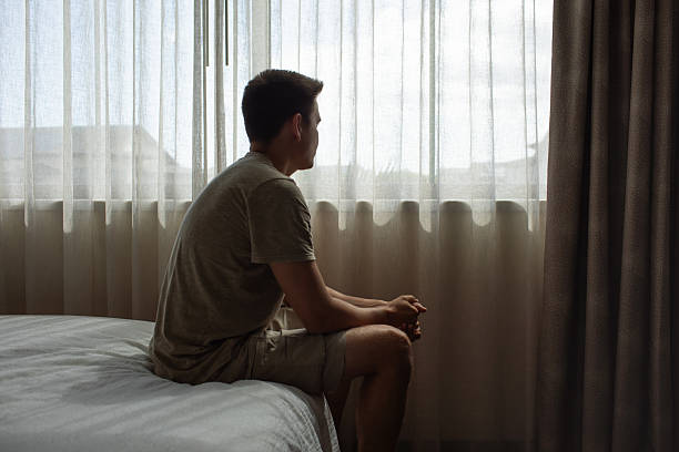 istock Thoughtful alone man in his bedroom looking out his window thinking about life 2230856842