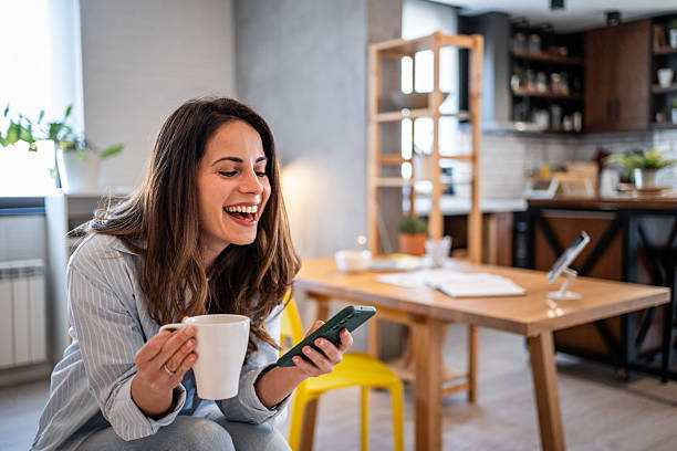 istock Young woman laughing while reading a text message and drinking coffee in her modern apartment 2230862224
