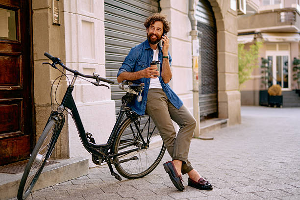 istock Stylish man talking on the phone while sitting on his bicycle and drinking coffee 2230863967