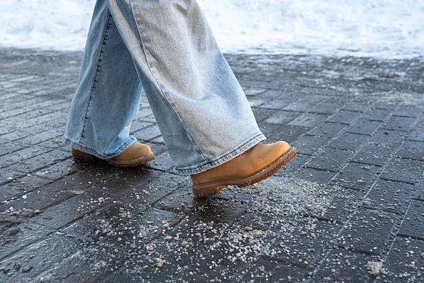 Anti-icing chemicals in winter season. Man walking on the street treated with technical salt or de-icing chemicals. Effective tool to fight ice on surfaces. Rock salt on road.