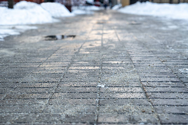 Road surface treated with technical salt to prevent ice formation, salt puddles on the road. Snow removal and maintenance of footpaths in winter time