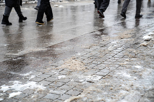 Anti-icing chemicals in winter season. People walking on the street treated with technical salt or de-icing chemicals. Effective tool to fight ice on surfaces. Rock salt on road.