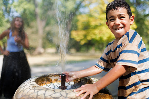 A smiling boy playing with a water fountain during a bright day in a park, embracing joy and refreshment outdoors.
